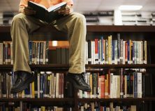 Man Reading Book and Sitting on Bookshelf in Library